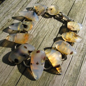 May include: A silver bracelet with agate stones in shades of brown, white, and gray. The stones are cut into irregular shapes and are connected by silver links.
