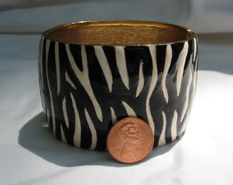 Increíble brazalete con bisagras de 1 ¾" de ancho, con diseño de cebra, firmado por CINER, esmaltado en blanco y negro, ideal para la pasarela de los años 80.