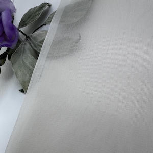 Peut inclure: Tissu blanc transparent avec une texture fine en maille. Le tissu est lisse et délicat, avec un léger brillant.
