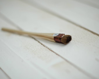 May include: A small wooden paintbrush with brown bristles and a leather handle. The handle has a white label with the number "7" on it.