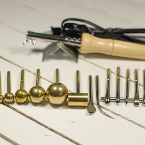 May include: A set of leather crafting tools including a soldering iron with a wooden handle, a variety of round metal tips, and several metal tools with different shapes.