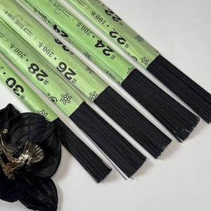 Peut inclure: Cinq paquets de fil de fer noir fin pour fleurs, enveloppés dans des étiquettes en papier vert clair. Les étiquettes portent les inscriptions #22, #24, #26, #28 et #30, ainsi que des caractères japonais et des quantités. Une fleur en tissu noir est placée en bas.