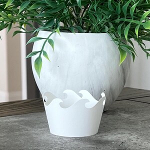 May include: White cupcake liner with a wave design. The liner is sitting on a gray surface.