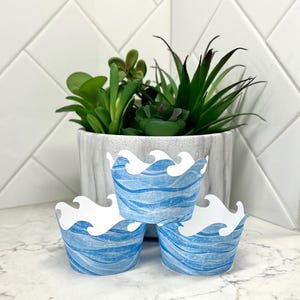 May include: Three blue and white cupcake liners with a wave design. The liners are stacked on top of each other.