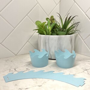 May include: Two light blue cupcake wrappers with a wave design and a matching light blue cupcake wrapper band.