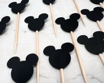 May include: A set of 12 black Mickey Mouse head cupcake toppers with wooden sticks. The toppers are made from black cardstock and are ideal for adding a touch of Disney magic to your next party.