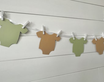 May include: A string of baby onesies in green and brown, hanging on a white string with clothes pegs.