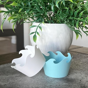 May include: Two cupcake wrappers with a wave design. One is white and the other is light blue.