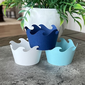 May include: Three cupcake liners with a wave design. The liners are blue, white, and light blue.