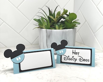 May include: Two light blue place cards with black borders and Mickey Mouse head accents. One card reads "Hey Diggity Dogs" in black script. A potted succulent plant sits in the background.