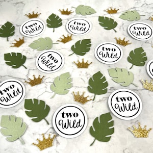 May include: Green and white confetti with gold crowns and circles that say "two wild" in black text.