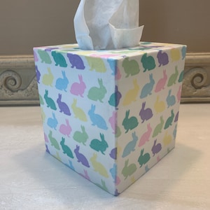 May include: A white tissue box cover with a pastel bunny rabbit pattern. The box is square and has a white tissue box inside.