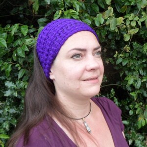 May include: A vibrant purple crocheted headband. The headband is worn on the head and is made of a textured, woven material. The person in the image is wearing a purple shirt and has long brown hair.