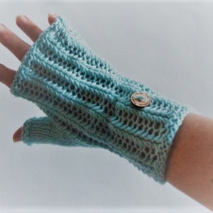 Könnte beinhalten: Hellblauer Fingerhandschuh mit strukturiertem Strickmuster. Der Handschuh hat einen Holzknopfverschluss und bedeckt die Hand bis zu den Knöcheln. Der Handgelenkbereich ist gerippt. Der Handschuh ist aus weichem, möglicherweise Wollmaterial.