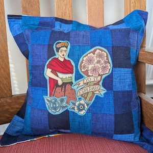 May include: Square blue plaid pillow with a Frida Kahlo-inspired design. The pillow features an illustration of a woman with flowers in her hair, a red shawl, and a bouquet of flowers with the text "YO TE ESPERARE". Additional floral and rose designs are also present.