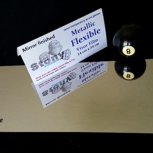 May include: A sheet of silver chrome metallic flexible visor film, 14 inches by 34 inches, with a mirror finish. The film is shown on a black surface with a black 8-ball and its reflection.