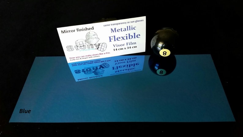 May include: A blue, mirror-finished, flexible visor film sheet with the text "Metallic Flexible Visor Film 14 cm x 34 cm" and a drawing of a person wearing a visor. The sheet is next to a black 8-ball with a yellow number 8.