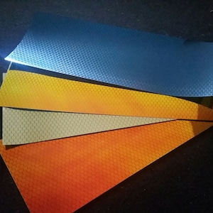 Könnte beinhalten: Vier Blätter reflektierendes Material in verschiedenen Farben: Orange, Beige, Gelb und Blau. Jedes Blatt hat ein sechseckiges Muster.