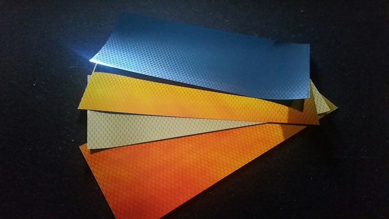 May include: Four sheets of reflective material in different colours: orange, beige, yellow, and blue. Each sheet has a hexagonal pattern.