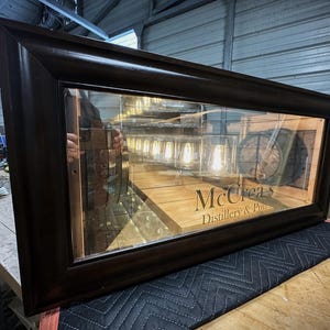 May include: A dark brown framed display case with a glass front. The interior features a wooden surface with the text "McCreas Distillery & Pub". Inside, there are several lit light bulbs and a barrel.
