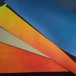 May include: Four sheets of reflective material with a honeycomb pattern. The sheets are in shades of orange, yellow, grey, and blue.