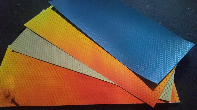 May include: Four sheets of reflective material with a honeycomb pattern. The sheets are in shades of orange, yellow, grey, and blue.