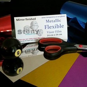 May include: A red, blue and gold metallic flexible visor film with a mirror finish. The film is 14 cm by 34 cm and comes with a pair of scissors. The product packaging includes the text "Mirror finished", "Stony", "Metallic Flexible Visor Film", "14 cm x 34 cm", and "same transparency as sun glasses".
