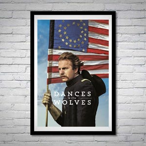 May include: A framed movie poster for "Dances with Wolves" featuring a man in a military uniform holding an American flag. The flag has red and white stripes and a blue field with stars. The movie title is displayed in white text.