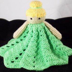 May include: A crocheted doll with a green dress and yellow hair. The doll is attached to a green crocheted blanket.