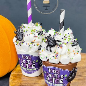 May include: Two chocolate cups filled with white frosting, marshmallows, and sprinkles. The cups are decorated with black beetle figurines and purple labels that read "100% Beetle Juice Freshly Squeezed".