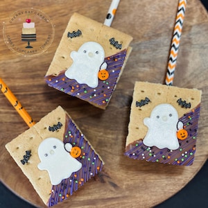 May include: Three graham cracker treats decorated with white ghost shapes, purple and brown icing, and sprinkles. The treats are on a wooden surface and each has a straw.