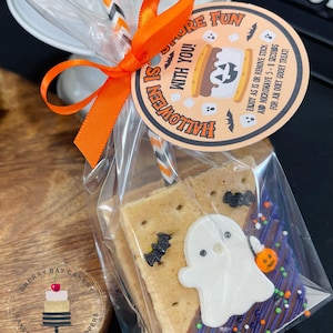 May include: A clear plastic bag filled with a s'mores treat decorated with a ghost and bats. The treat is tied with an orange ribbon and a tag that says "Halloween is with you! Enjoy as is or remove stick and microwave 5-8 seconds for an ooey gooey treat!"