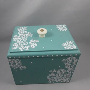 May include: A teal wooden box with a white knob on the lid. The box is decorated with white swirls and dots.