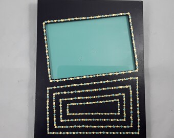 May include: A black picture frame with a teal blue mat and a decorative border of yellow and blue dots.