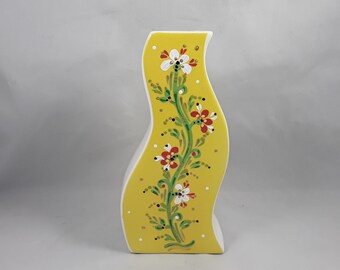 Könnte beinhalten: Eine gelbe Keramikvase mit wellenförmigem Design und einem floralen Muster, das in Rot, Weiß und Grün bemalt ist.