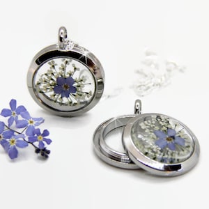 May include: Two silver locket necklaces with a clear glass insert. The locket contains pressed forget-me-not flowers and white baby's breath.