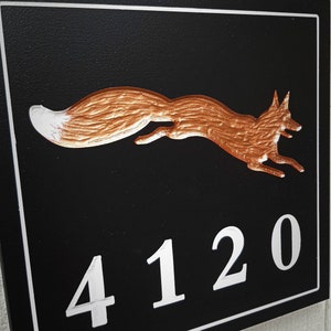 K&ouml;nnte beinhalten: Ein schwarzes Hausnummernschild mit wei&szlig;em Rand. Das Schild zeigt eine kupferfarbene Fuchs-Silhouette und die Nummer 4120 in Wei&szlig;.