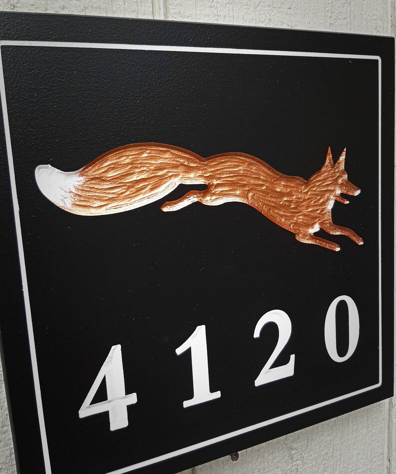 K&ouml;nnte beinhalten: Ein schwarzes Hausnummernschild mit wei&szlig;em Rand. Das Schild zeigt eine kupferfarbene Fuchs-Silhouette und die Nummer 4120 in Wei&szlig;.