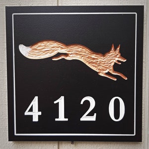 K&ouml;nnte beinhalten: Ein schwarzes Holzschild mit wei&szlig;em Rand und einer kupferfarbenen Fuchs-Silhouette. Die Nummer 4120 ist in Wei&szlig; auf das Schild geschnitzt.