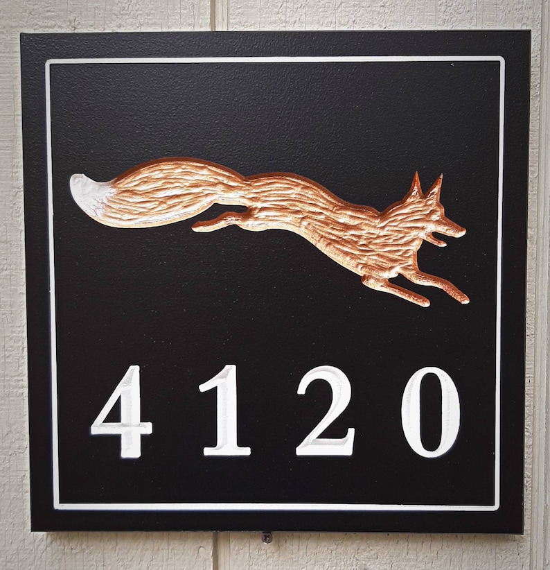 K&ouml;nnte beinhalten: Ein schwarzes Holzschild mit wei&szlig;em Rand und einer kupferfarbenen Fuchs-Silhouette. Die Nummer 4120 ist in Wei&szlig; auf das Schild geschnitzt.