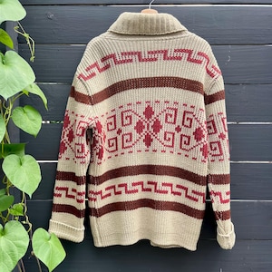 May include: A beige knitted cardigan with a brown and red geometric pattern. The cardigan has a collared neckline and long sleeves.