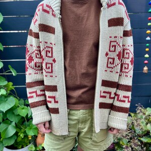 May include: A cream-coloured cardigan with a brown and red geometric pattern. The cardigan has a zip closure and a collar.