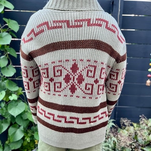 May include: A beige knitted sweater with a brown and red geometric pattern. The sweater has a high collar and long sleeves.