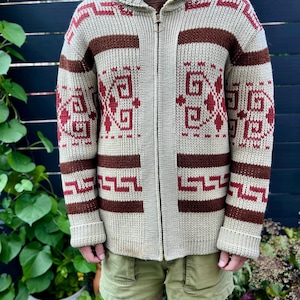 May include: A cream-coloured knitted cardigan with a brown and red geometric pattern. The cardigan has a zip closure and a collared neckline.