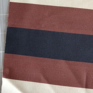 May include: A woven fabric featuring a repeating horizontal striped pattern. The design consists of wide bands in cream, followed by a thick stripe of dark brown, a central stripe of dark navy blue, and another thick stripe of dark brown.