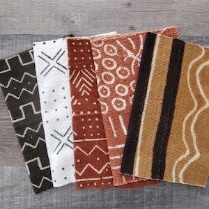 Op de afbeelding: Vijf stoffen stalen met patronen in zwart, wit en bruintinten. Elke staal heeft een uniek geometrisch ontwerp, waaronder zigzags, kruisen, stippen en strepen. De stoffen zijn gerangschikt op een verweerd houten oppervlak.