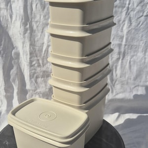 May include: A collection of beige plastic food storage containers with lids. The containers are rectangular with rounded edges and a ridged design. The lids are flat with a circular indentation. The containers are on a dark, round surface.