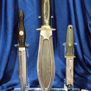 Puede incluir: Tres cuchillos en exhibición. El cuchillo central tiene una hoja larga plateada y un mango de madera. El cuchillo de la izquierda tiene un mango negro y una hoja plateada. El cuchillo de la derecha tiene un mango verde y una hoja plateada. El texto "Create Own Day" es visible.