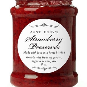 May include: A glass jar with a green lid filled with red strawberry preserves. The label reads "Aunt Jenny's Strawberry Preserves" and includes the text "Made with love in a home kitchen strawberries from my garden, sugar & lemon juice 8 oz."