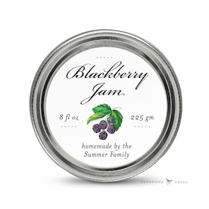 May include: A white jar lid with a label that reads "Blackberry Jam" in cursive script. The label also includes a watercolor illustration of blackberries and leaves, along with the text "8 fl oz", "225 gm", and "homemade by the Summer Family".